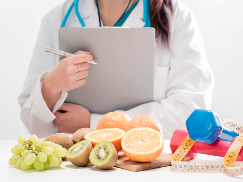 Doctor holding clipboard in front of fruit and weights discussing nutrigenomics