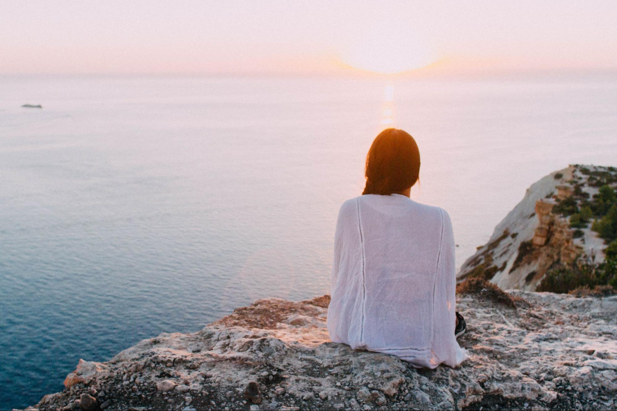 Woman on cliff watching sunrise contemplating physical wellness