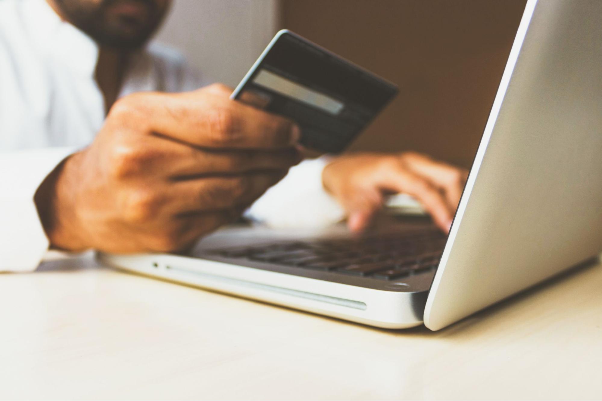 Hand holding credit card near laptop