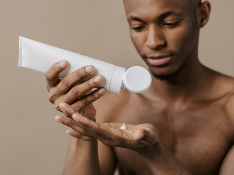 Black man holding tube of skin lotion above hand