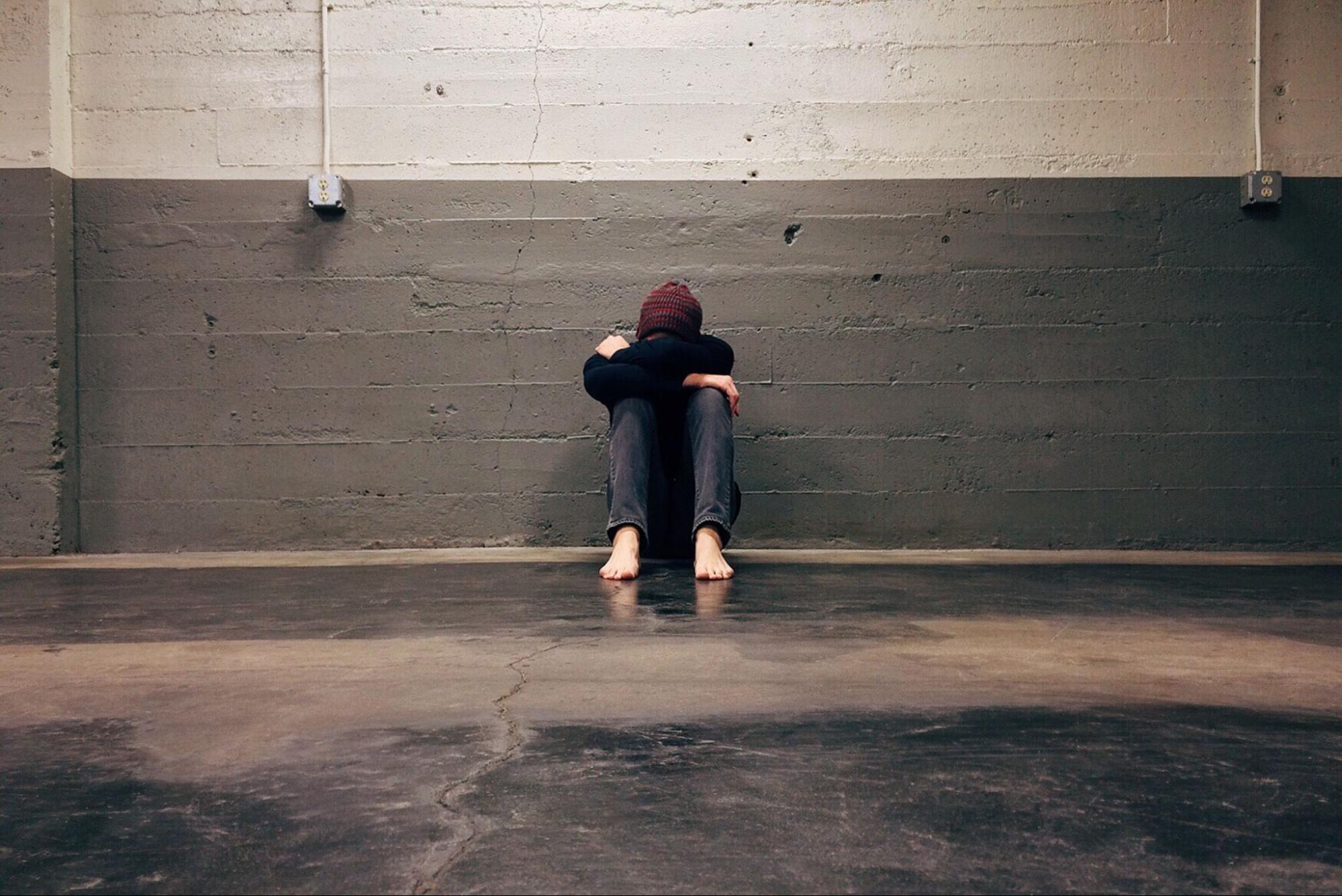 Person sitting barefoot with head in lap suffering from mild depression